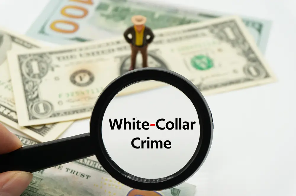 Magnifying glass highlighting the words 'White-Collar Crime' over a background of banknotes and coins, representing financial crime and business-related fraud.
