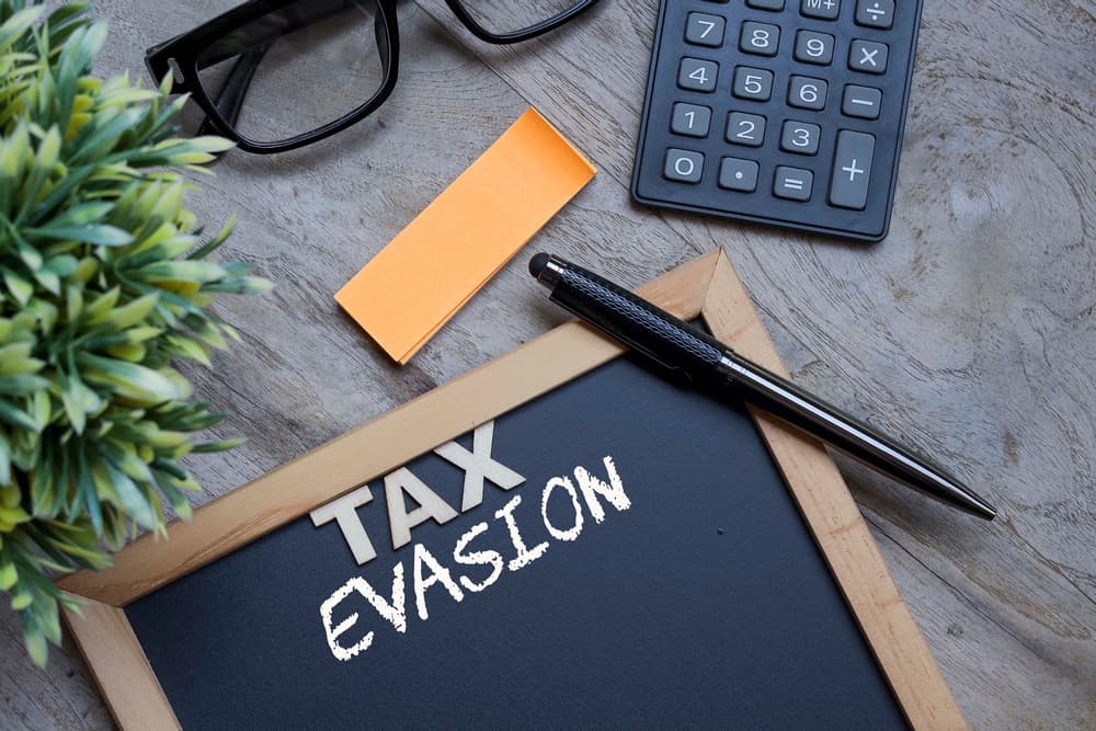 Black chalkboard with letterings on TAX EVASION. Pen, sticky note, calculator and eyeglasses.