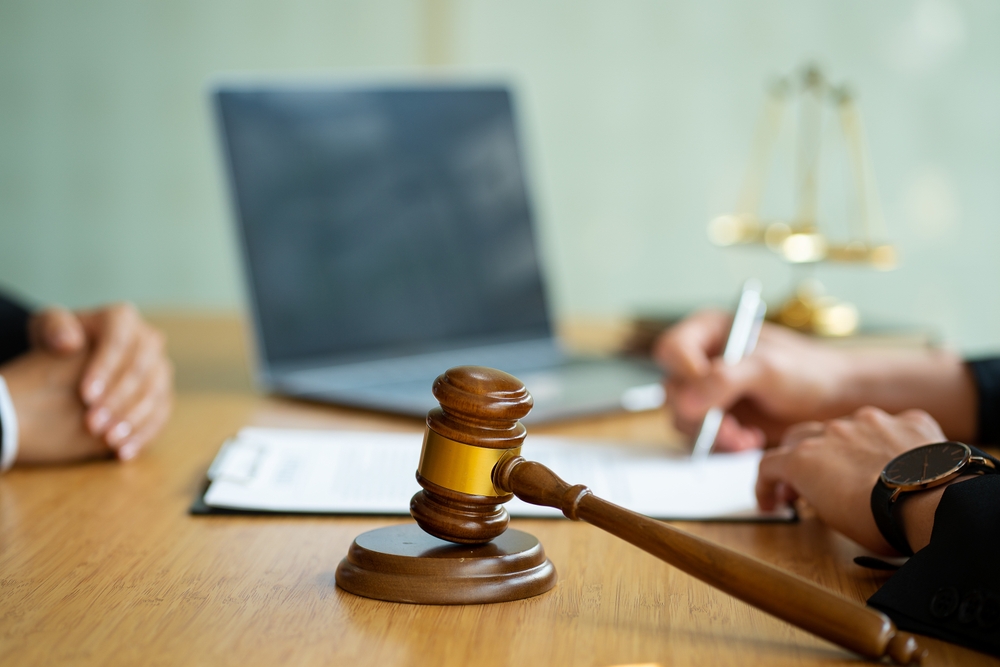 Male businessman and lawyer meeting with a client team in an office, discussing and signing a legal contract, with a judge’s gavel and scales of justice on the table, symbolizing legal services and consultation.